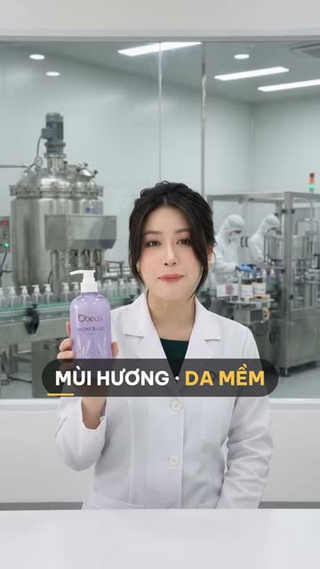Chuyên viên BECO cầm chai sữa tắm "Shower Gel" màu tím có vòi bơm, phía sau vách kính là bồn khuấy lớn và dây chuyền chiết rót chai vòi bơm