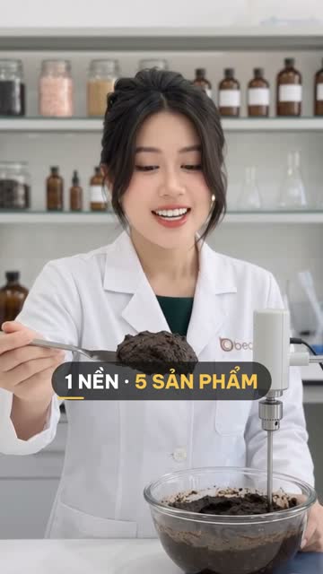 Chuyên viên BECO múc thìa nền tẩy tế bào chết màu nâu đậm từ tô thuỷ tinh có máy khuấy, phía sau là kệ hũ hạt và chai thuỷ tinh nâu trong phòng lab
