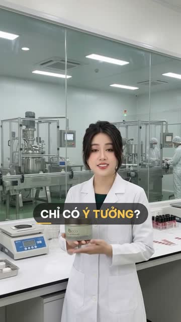 Chuyên viên BECO mặc áo blouse trắng cầm hũ kem mẫu nhãn "your brand" trong phòng lab, phía sau vách kính là dây chuyền pha chế và chiết rót