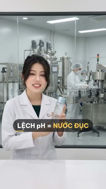 Chuyên viên BECO cầm chai toner nắp bạc, phía sau vách kính là bồn khuấy inox, hệ thống lọc và công nhân đứng ở dây chuyền chiết rót chai