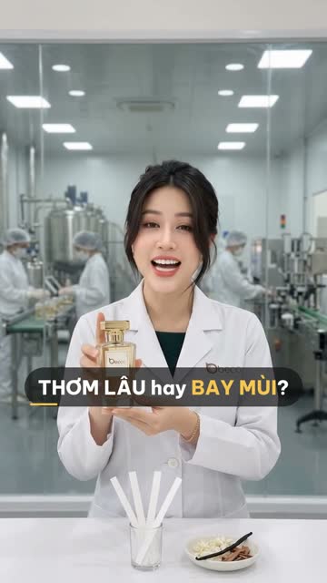 Chuyên viên BECO cầm chai nước hoa nắp vàng, trên bàn có cốc que thử mùi và đĩa nguyên liệu hương, phía sau vách kính là bồn inox và công nhân ở dây chuyền chiết rót