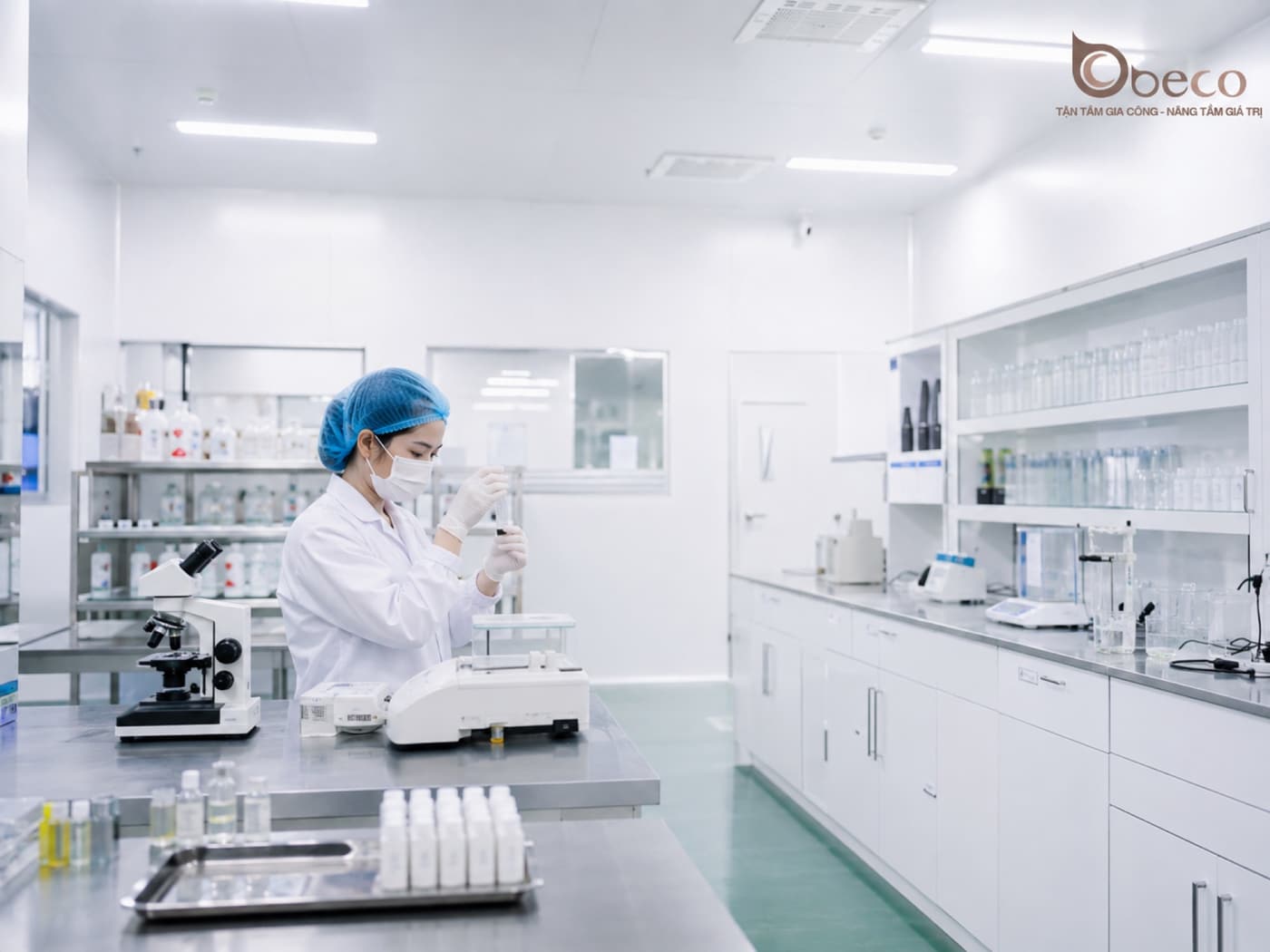 Chuyên viên phòng lab BECO thao tác mẫu thử bên kính hiển vi và cân phân tích, khay chai mẫu đặt sẵn trên bàn inox
